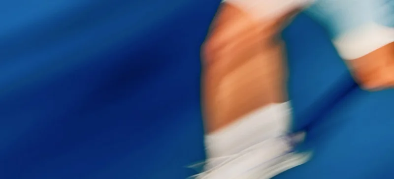 Motion-blurred tennis player in action against a blue court background.