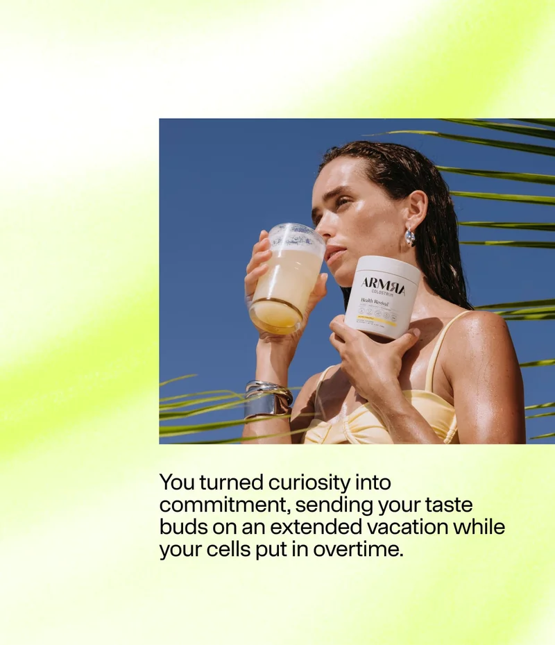 Woman holding a glass drink and an ARMRA Colostrum container outdoors with palm leaves and blue sky.