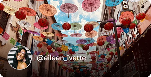 Image Description: Colorful umbrellas hanging on clotheslines. A profile photo of a person smiling and the handle @eileen_ivette is on the bottom left corner of the image.