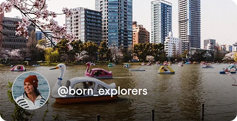 Image Description: A lake with swan boats surrounded by skyscrapers and cherry blossoms. A profile photo of a person wearing a red hat and the handle @born_explorers is on the bottom left corner of the image.