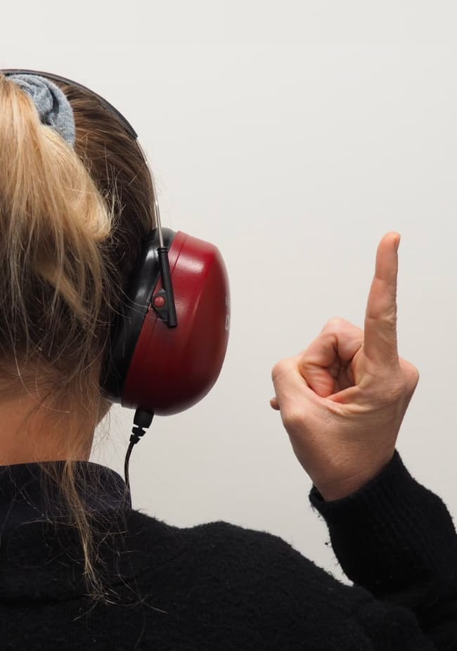A woman wearing over-the-ear headphones holds one finger in the air.
