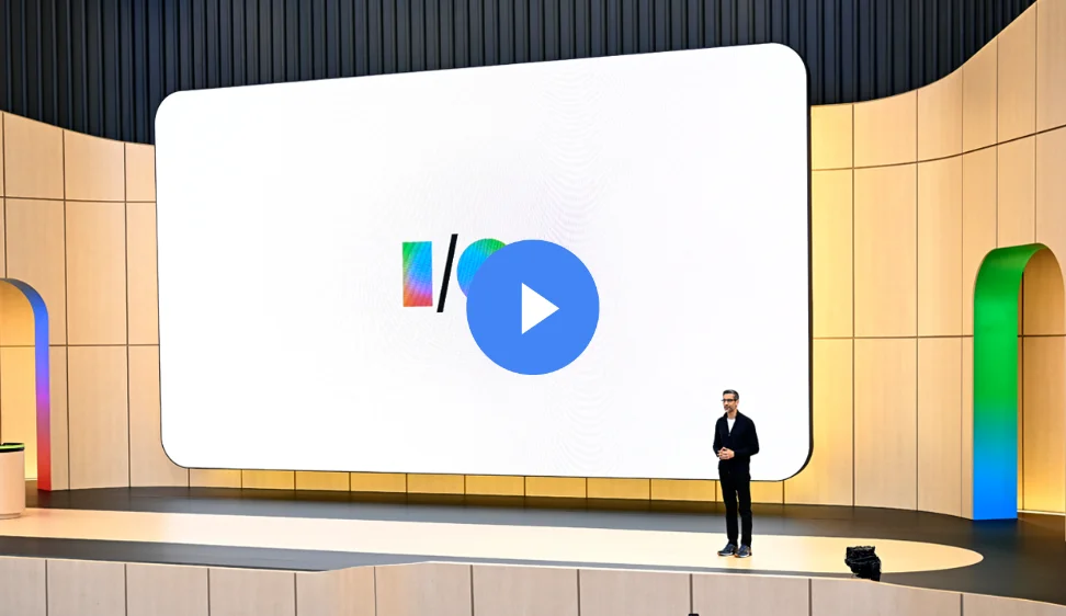 Sundar Pichai on a Google I/O stage with a large logo screen and a colorful arched doorway.