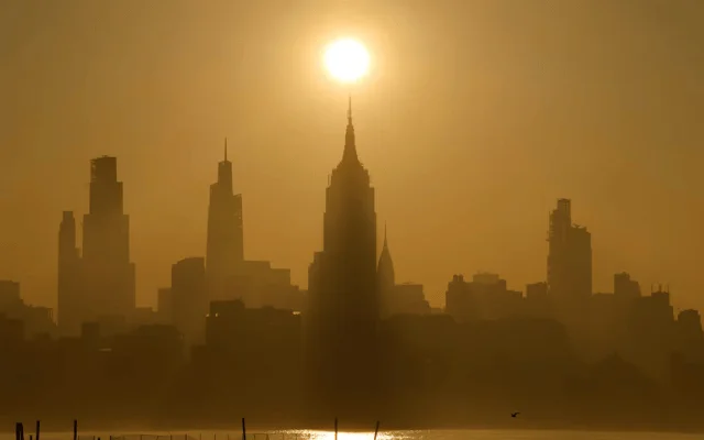 The sun rises behind the skyline of midtown Manhattan and the Empire State Building in New York City.