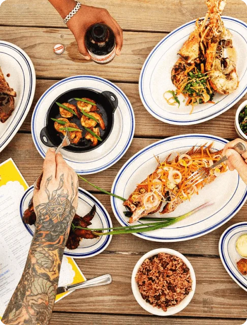 Image Description: Flatlay of travelers enjoying grilled seafood and beer at a restaurant in Jamaica