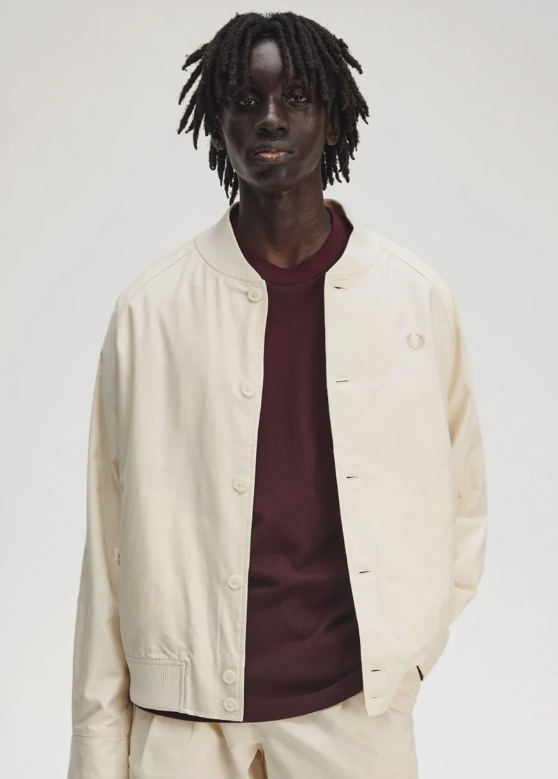 A black male model wears a Fred Perry Twill Tennis Jacket in Ecru