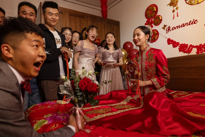 A woman wearing a beautiful red outfit sits as her friends and family gather around her