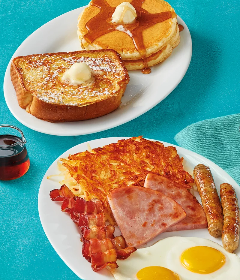 Two eggs served your way, two pork sausage links, two slices of thick-cut ham, two strips of hickory-smoked bacon, and hash browns on a plate. Served with 2 buttermilk pancakes topped with syrup and butter, along with a slice of Classic Thick 'N Fluffy French
 Toast.