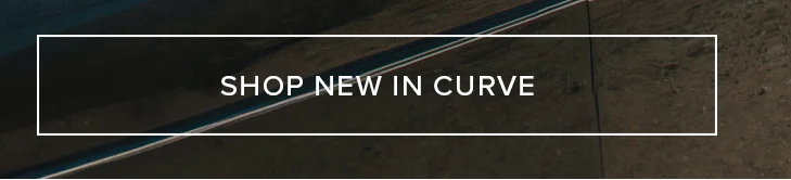 Aerial view of dark asphalt road with white lines winding through a rugged, brown landscape. Shop the new Curve collection arrivals.