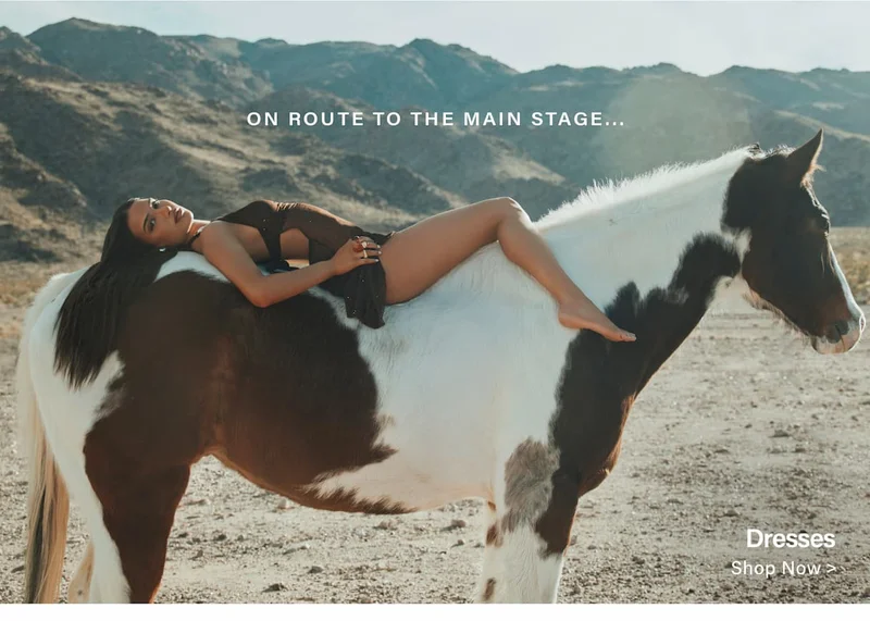 Woman in a sheer cutout dress lounging on a brown and white pinto horse in desert mountains. Shop unique festival dresses now.