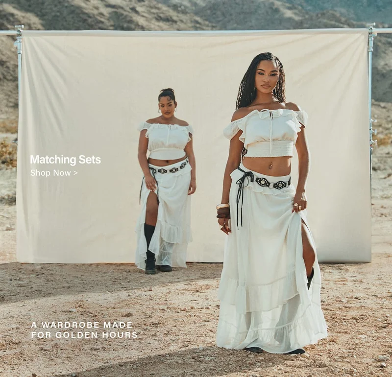 Two women model white ruffled boho matching sets with black belts in a desert, promoting chic two-piece desert fashion for golden hours.