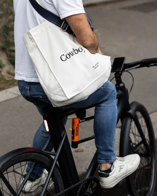 A photograph. A close up of a cyclist holding a Cowboy tote bag