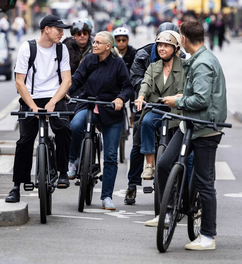 A photograph. A large group of cyclists on Cowboy bikes gather together on a Paris street.