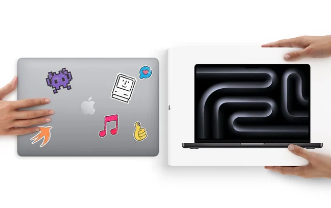 Used MacBook Pro, silver color, closed lid covered in various stickers, being traded in for a new MacBook Pro, space black color, with Liquid Retina XDR display in box