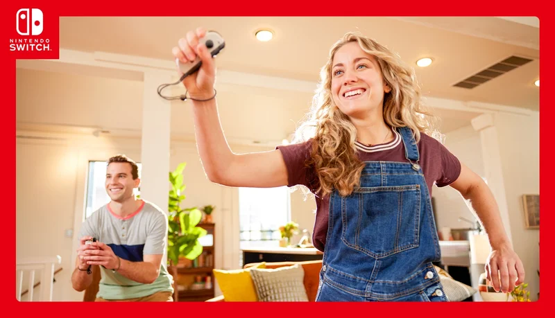 Two people, with big smiles on their faces, are in active poses while playing a Nintendo Switch game using motion controls. Each of them is holding a single Joy-Con Controller.