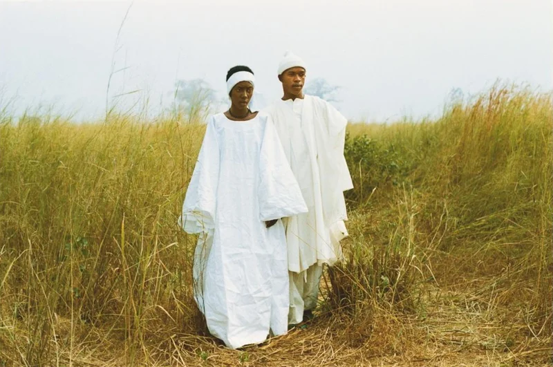 Two people wearing white robes walking through tall grass