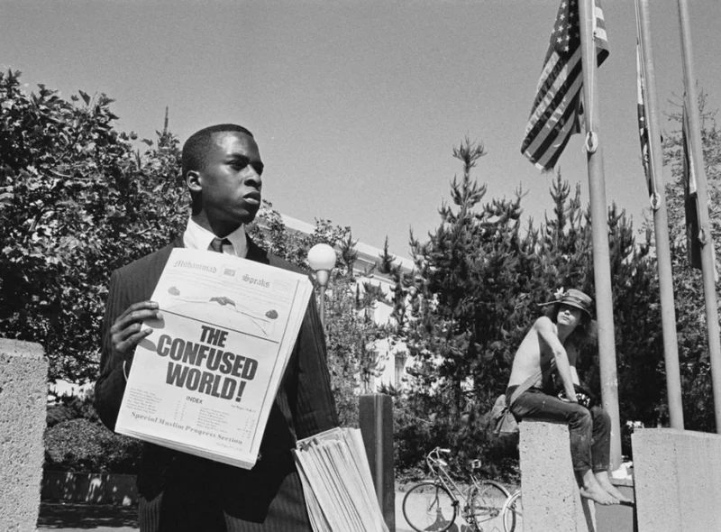 A Black man in a suit holding a newspaper with the heading “The Confused World!”