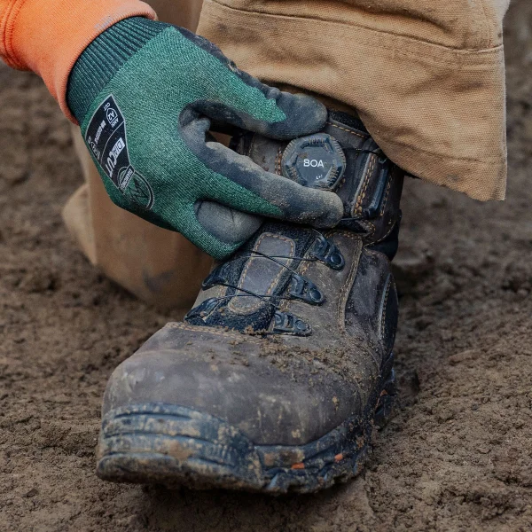A worker wearing gloves adjusts the BOA® dial on a muddy Vicious BOA® work boot.