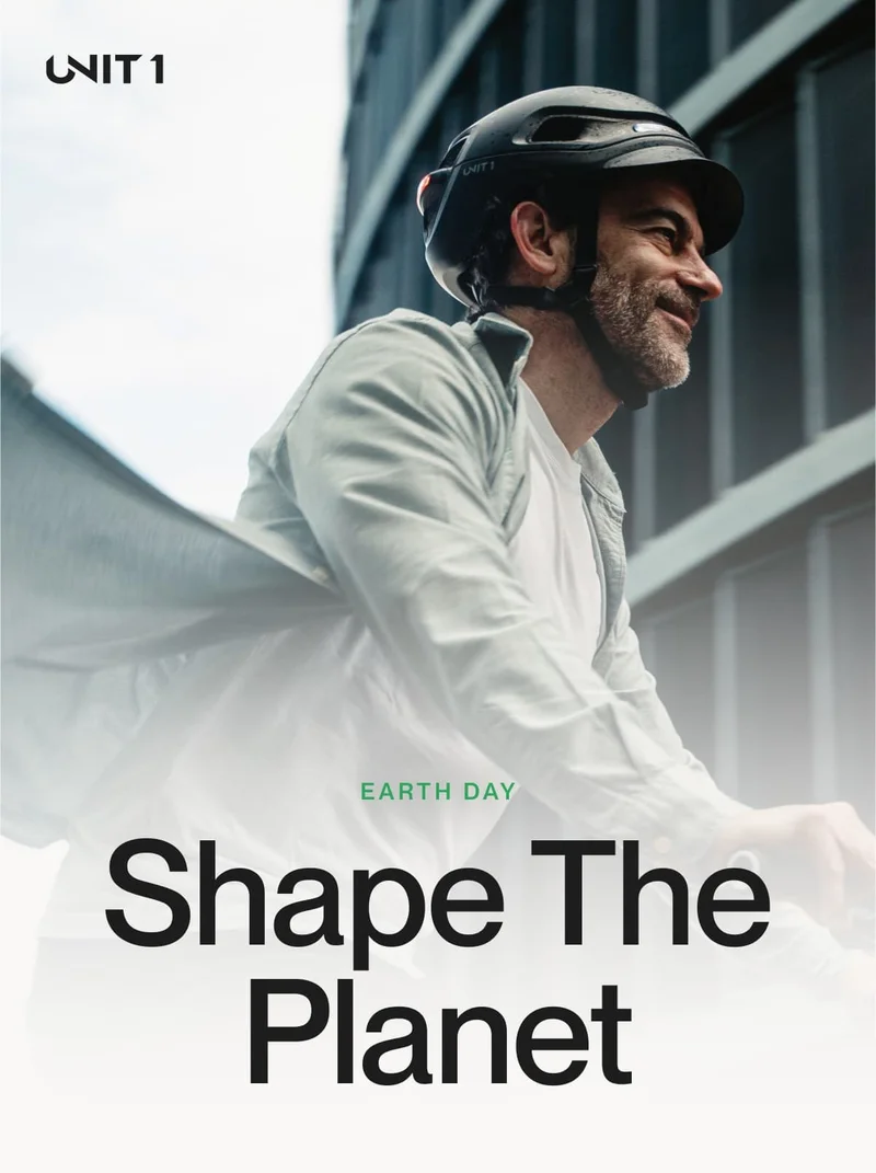 A man smiling while cycling in an urban environment with his UNIT 1 helmet, under the message “Shape The Planet” — promoting smarter, sustainable commuting.