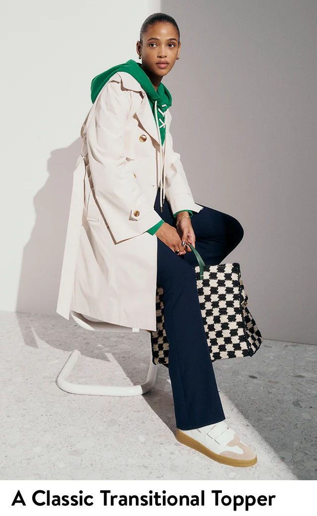 A woman wearing a trench coat with a green hoodie and blue pants.