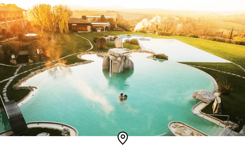 Image Description: Two travelers hugging in a giant thermal pool at a countryside spa resort in Tuscany, Italy
