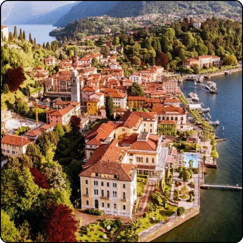 Image Description: Aerial view of a charming town that juts out onto the water. There are multiple orange-hued buildings with lots of trees throughout.