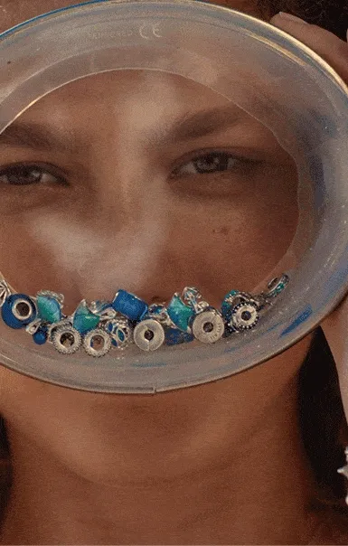 A model looks through a large goggle filled with blue and silver charms.