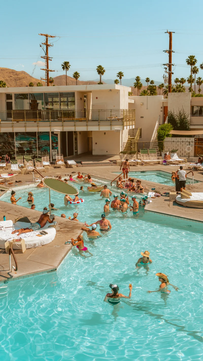 Guests enjoying a sunny day poolside at Ace Hotel Palm Springs, with mountains and palm trees in the background.