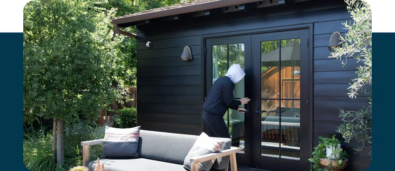 Burglar trying to enter a home. An Essential Outdoor Camera is mounted on the exterior.