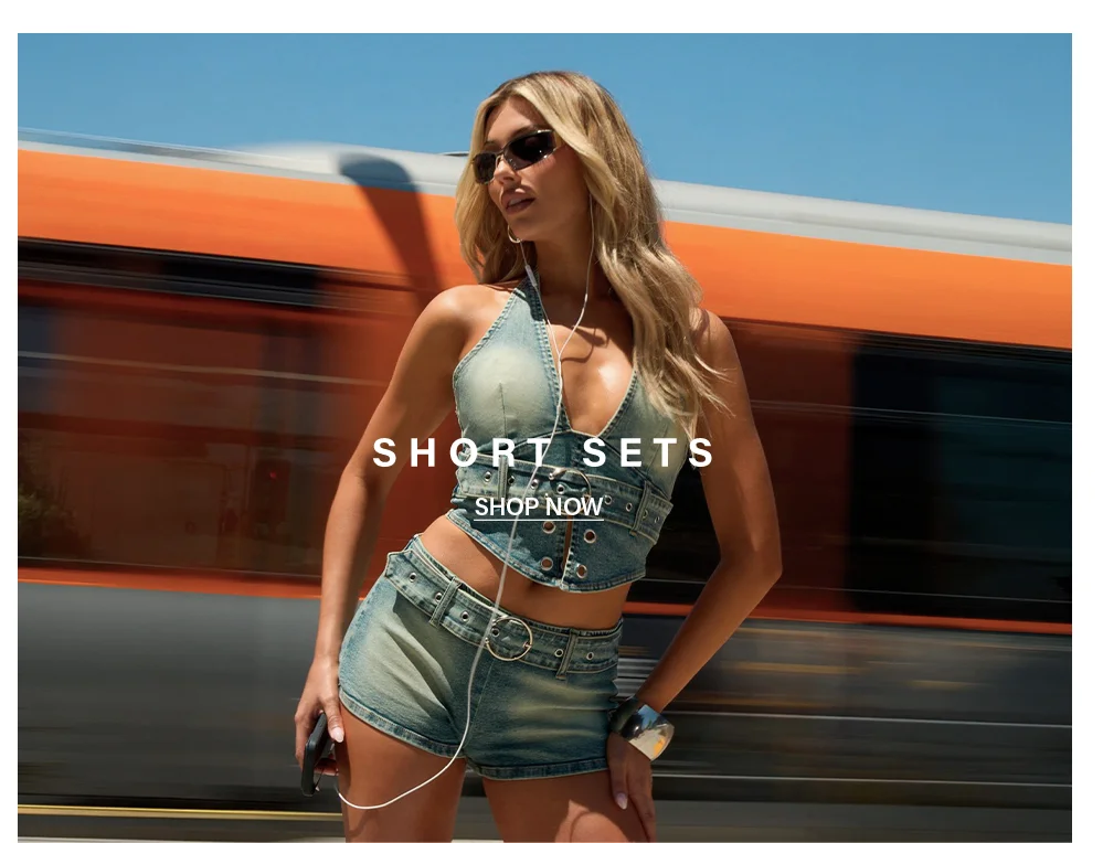 Blonde woman in trendy distressed denim halter top and matching shorts, by a blurred orange train.