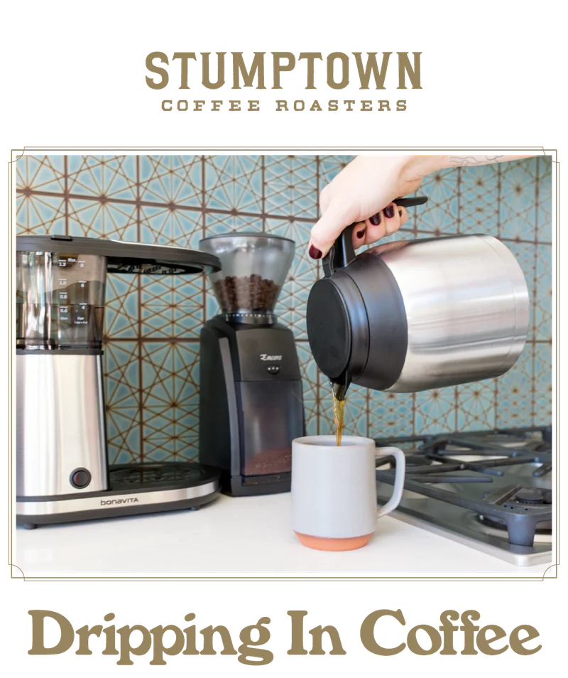Coffee poured into a mug beside a drip brewer and grinder. Text reads “Dripping In Coffee.”