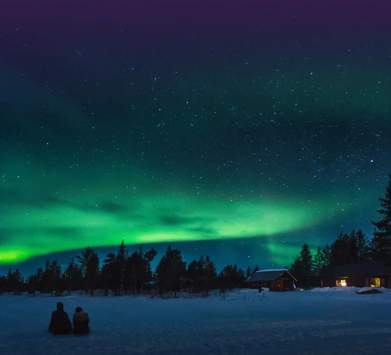 Image Description: Two travelers admiring the Northern Lights on a frozen lake in Sweden