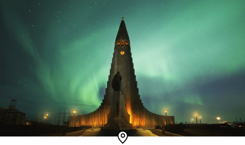 Image Description: Landscape shot of the Northern Lights dancing above the iconic Hallgrimskirkja Church in Reykjavík, Iceland