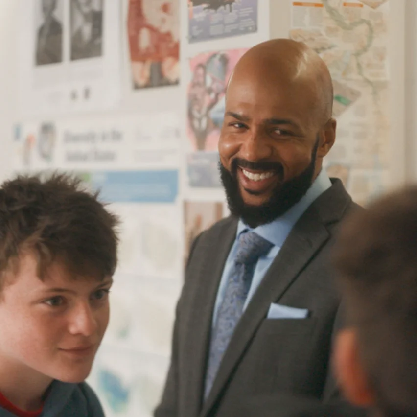 Smiling man in a suit and a student in a classroom.