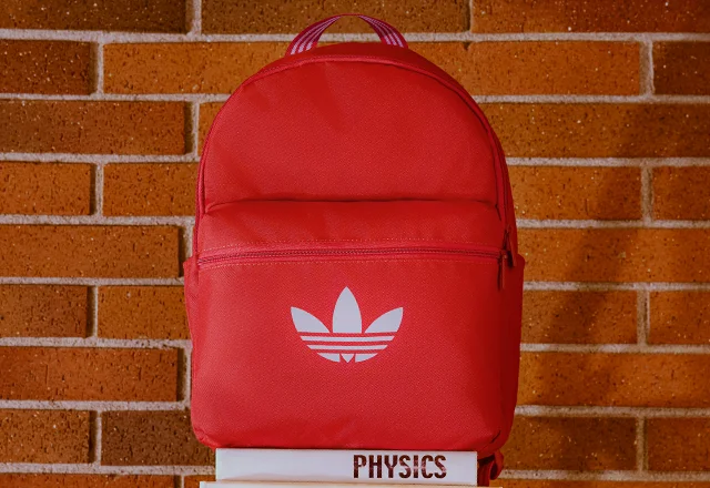 Red backpack with adidas logo, sitting on a stack of textbooks