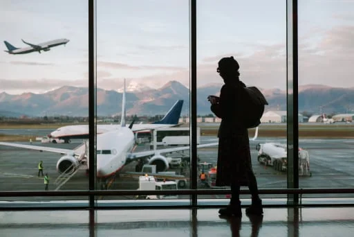 A traveler stands in an airport terminal watching a plane take off.