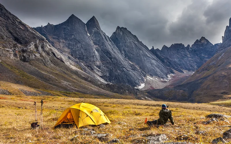 A camper gazes at the central Brooks Mountain Range, which includes East and West Maiden Peaks, Camel Peak, and Arrigetch Peaks—all found within Alaska’s Gates of the Arctic National Park and Preserve, one of America’s least-visited national parks.