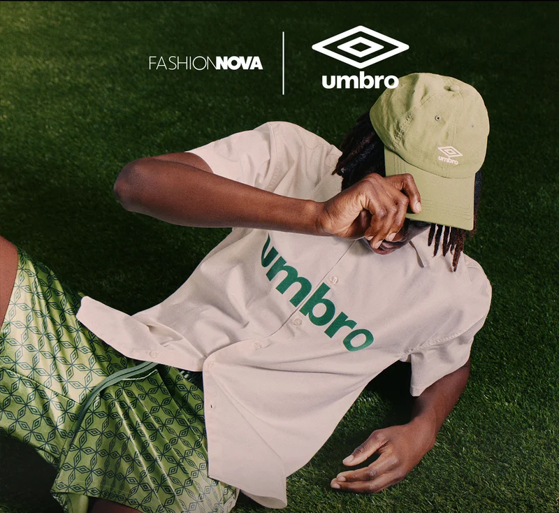 Fashion Nova x Umbro: Model in olive cap, beige Umbro shirt & green patterned shorts, on grass. Men's casual collection.