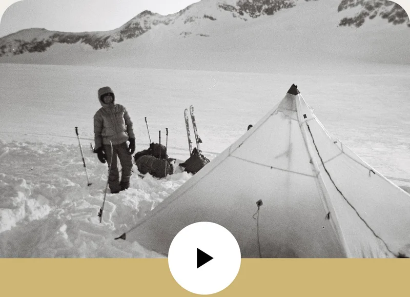 A person walking around in the snow outside of a tent.