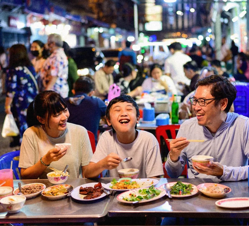 Image Description: A family enjoying street food along a busy street in Chinatown, Bangkok
