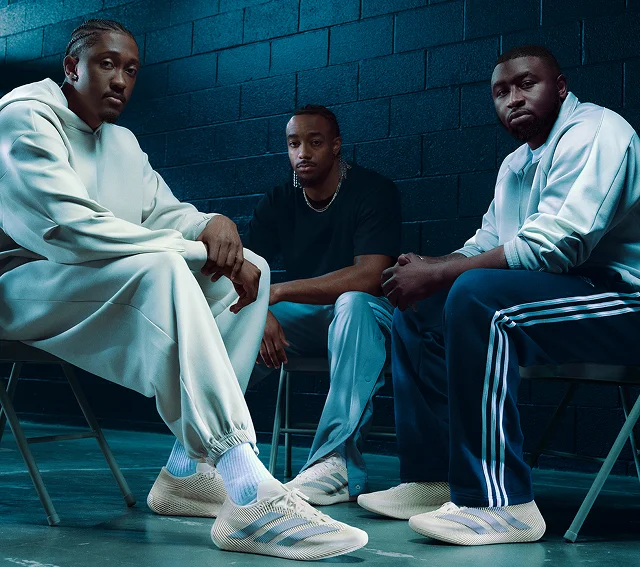 Jalen Williams and two men sit indoors against a dark wall, wearing casual adidas outfits and beige adidas Climacool Laced trainers.