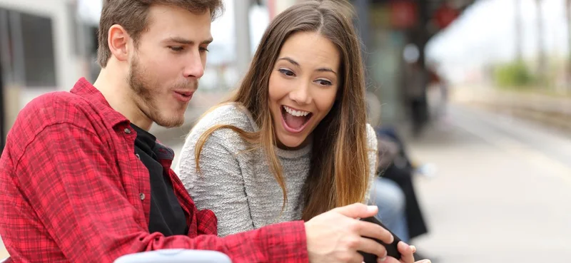 Funny couple playing games with a smart phone in a train station while they are waiting