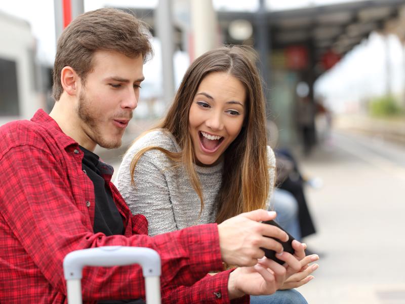 Funny couple playing games with a smart phone in a train station while they are waiting