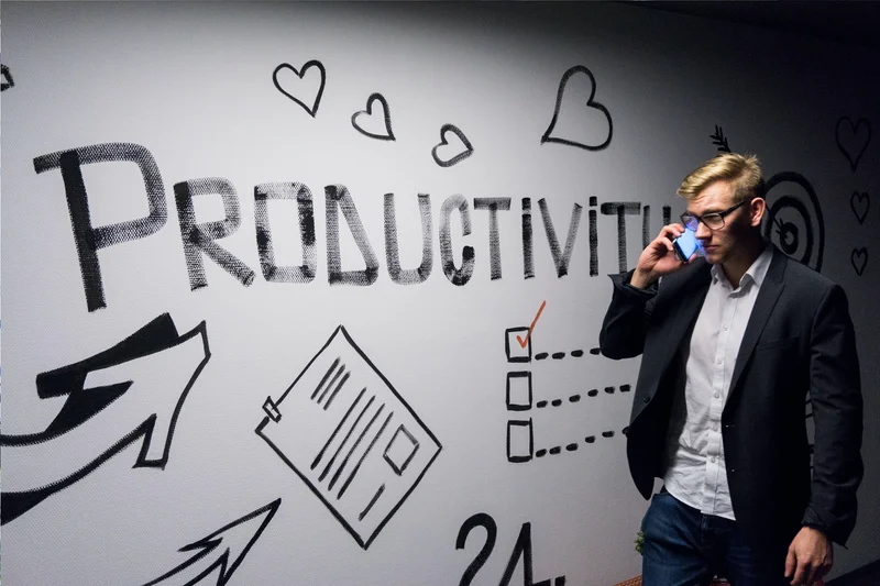 A man talking on a phone walks by a white wall with the word Productivity and doodles written in black.