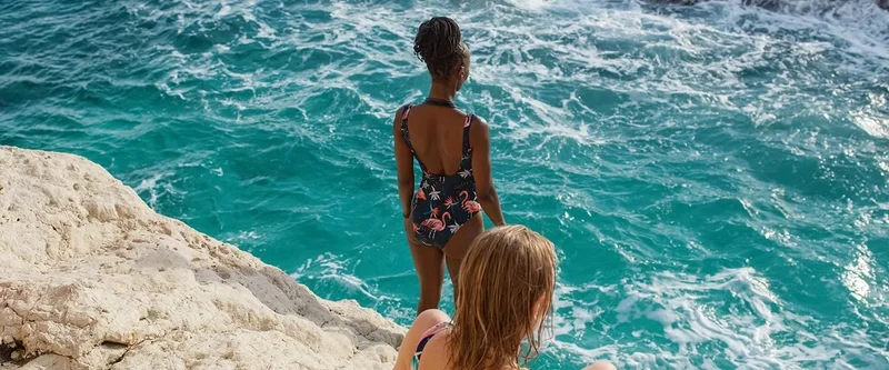 Two women on a rock look out over green-blue waters