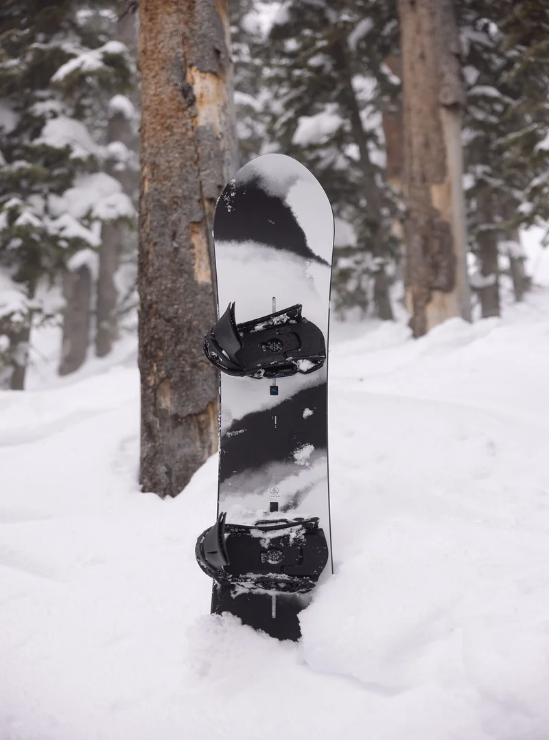 The Burton Family Tree Alekesam Camber Snowboard in the snow with trees in the background