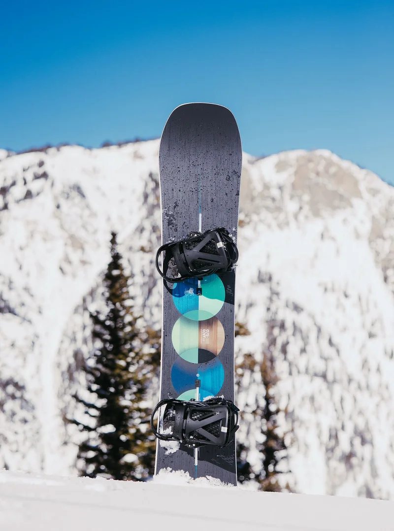 The Men's Burton Custom Camber Snowboard in the snow with a mountain in the backgroun