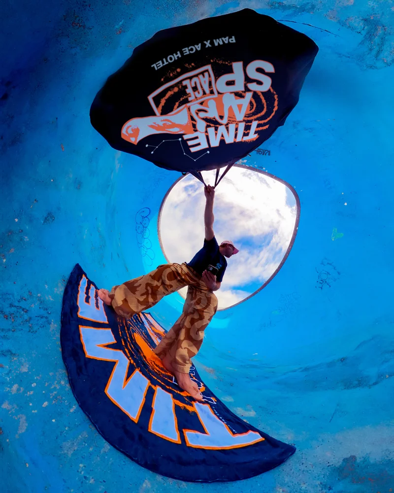 Animated image of a person mid-air, wrapped in cosmic-themed fabric with Ace Hotel branding, highlighting the P.A.M. collaboration and its exploration of inner and outer worlds.