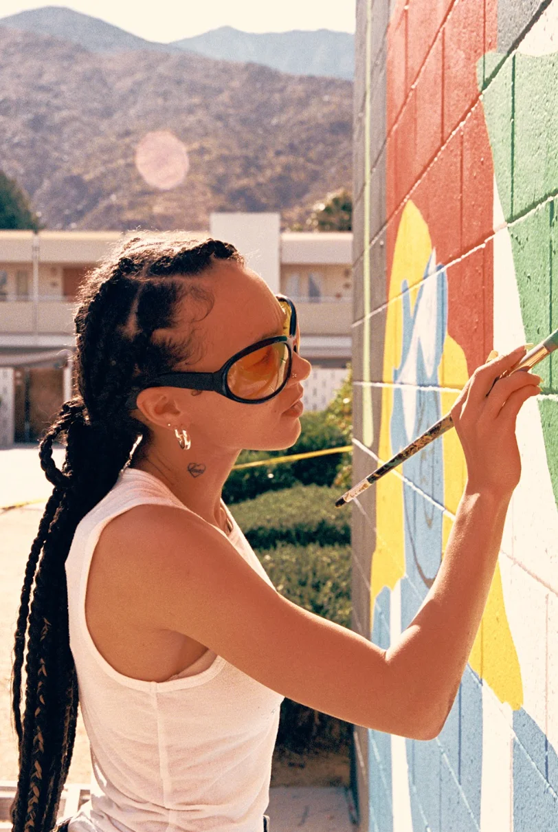 Corey Wash kneels in front of her vibrant mural at Ace Hotel Palm Springs, with artists working in the background.