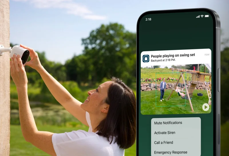 Person mounting an Arlo security camera on the exterior of a home. Phone with simulated screen image depicts an Arlo Secure notification that reads: People playing on swing set. Backyard at 2:18 PM. Mute notifications. Activate siren. Call a friend. Emergency response.