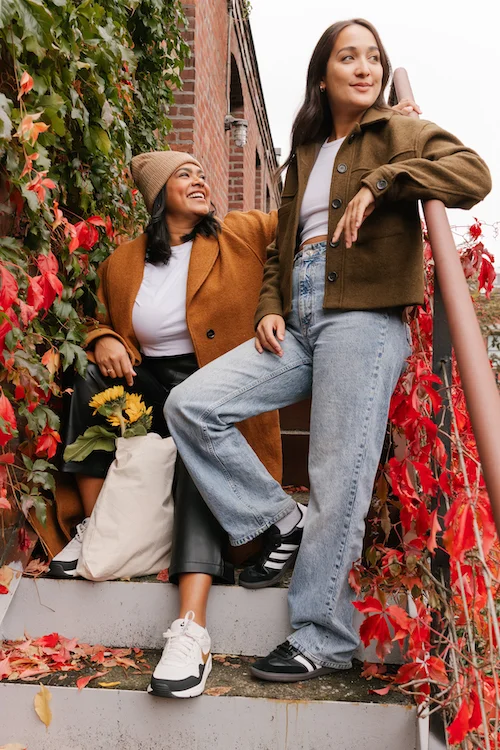 two women sat on steps of brick house surrounded by red leaves